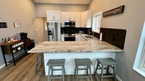 A modern kitchen with white cabinets, a large island with bar stools, stainless steel appliances, and a motivational quote on the wall. - Private RRG Retreat w/ Hot Tub & Game Room (Stanton)