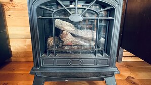 A black wood-burning stove with a glass front, set on a wooden floor in a room with wooden walls. - Lemhi Shoshone Cabin, Greyhouse Vacation Rentals (Salmon)