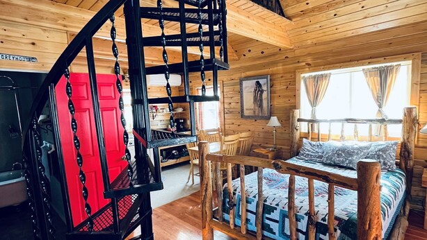 A cabin interior with a wooden staircase, a bed with a wooden frame, a dining area, and a kitchen. - Lemhi Shoshone Cabin, Greyhouse Vacation Rentals (Salmon)