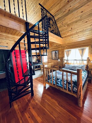 Interno di una baita con una scala in legno, un letto con struttura in legno, un'area pranzo e una cucina.