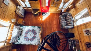 A cabin interior with a wooden floor, a red door, a spiral staircase, and a window with curtains. - Lemhi Shoshone Cabin, Greyhouse Vacation Rentals (Salmon)