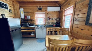 A compact kitchen with a refrigerator, microwave, and sink. There are wooden chairs and a table, and a window with curtains. - Lemhi Shoshone Cabin, Greyhouse Vacation Rentals (Salmon)