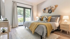 Une chambre à coucher comprenant un lit, des tables de chevet, une fenêtre avec des rideaux et un mur décoré d’assiettes.