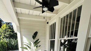 Une véranda couverte avec deux fauteuils à bascule en osier, un ventilateur de plafond et une plante en pot.