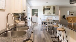 A modern kitchen with a granite countertop, stainless steel sink, and a dining area with a wooden table and bar stools. - Cozy and secluded getaway with hot tub & fireplace (Halifax)