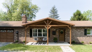A two-story house with a covered porch, a brick garage, and a front door with a welcome sign. - Cozy and secluded getaway with hot tub & fireplace (Halifax)