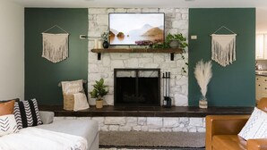 A living room with a stone fireplace, a mounted TV, and macramé wall hangings. - Cozy and secluded getaway with hot tub & fireplace (Halifax)
