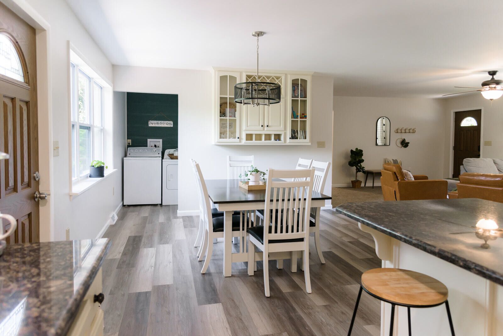 Une cuisine moderne avec des meubles blancs, une table à manger avec des chaises, un four encastré et un ventilateur de plafond.