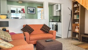 Een woonkamer met een oranje bank, een passende voetenbankje, en een afstandsbediening op het voetenbankje.
