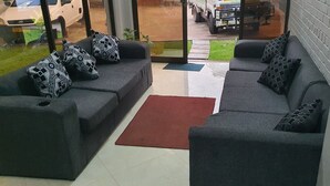 A living room with two grey sofas, patterned cushions, a red rug, and a glass door leading outside. - The Princess Guest House (Harare)
