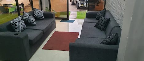 A living room with two grey sofas, patterned cushions, a red rug, and a glass door leading outside.