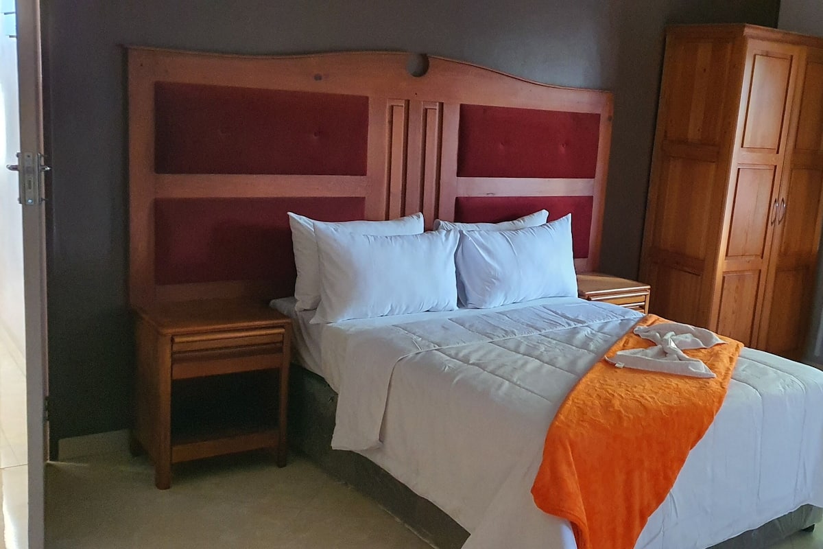 A hotel room with a wooden headboard, a bed with white bedding, two bedside tables, and a wardrobe.