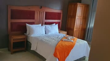A hotel room with a wooden headboard, a bed with white bedding, two bedside tables, and a wardrobe.