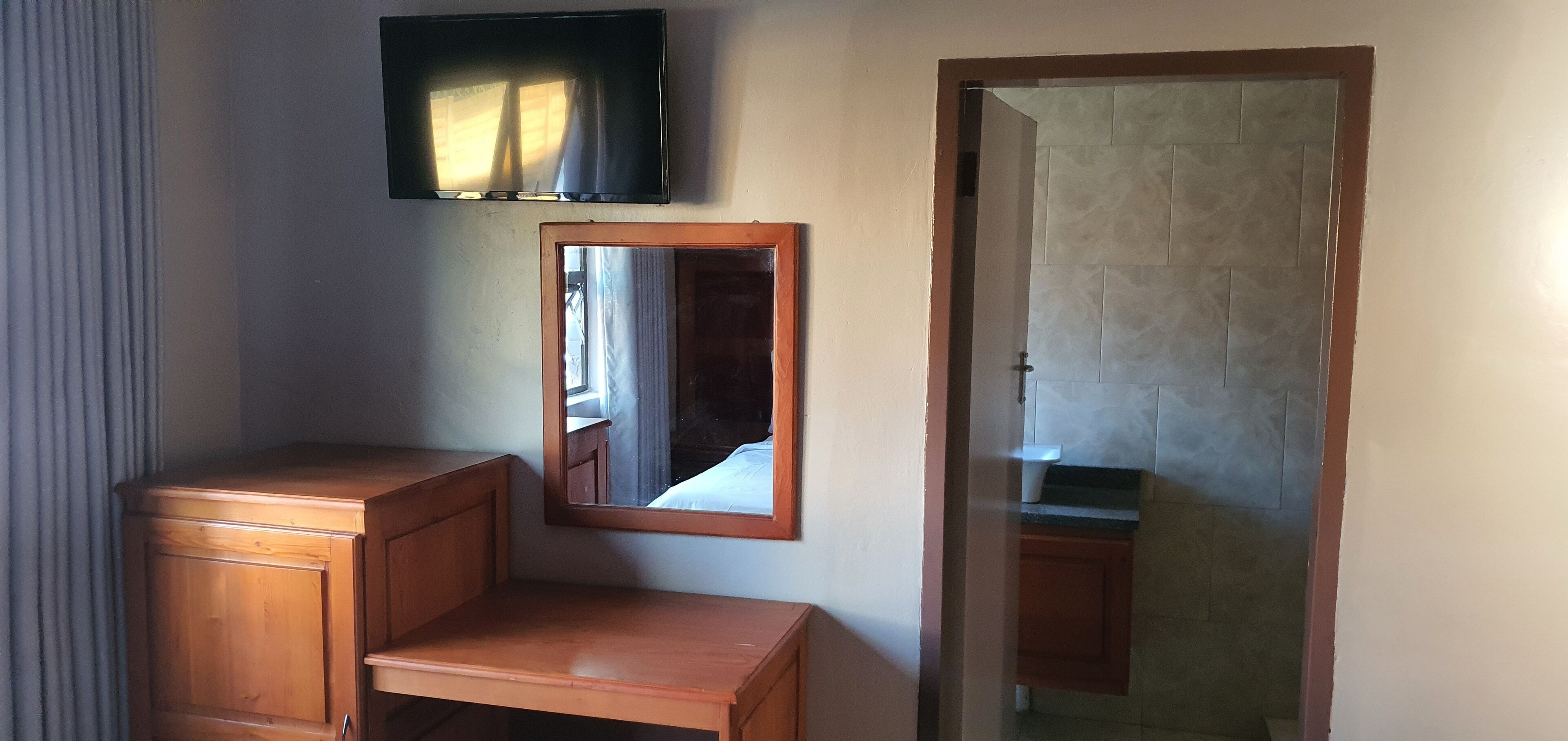 A room with a wooden cabinet, a mirror, and a television mounted on the wall.