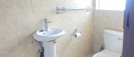 Un baño con lavamanos pedestal, inodoro y ventana que proporciona luz natural.