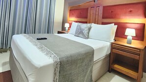 A hotel room with a large bed, two bedside tables with lamps, a headboard, and a window with curtains. - The Princess Guest House (Harare)
