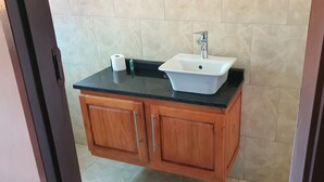 A bathroom with a white sink, black countertop, and wooden cabinets. - The Princess Guest House (Harare)