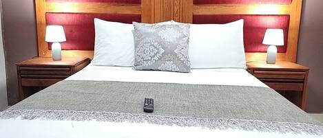 A hotel room with a large bed, two bedside tables with lamps, a headboard with a red panel, and a decorative pillow.