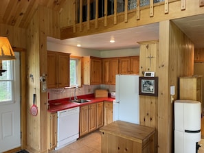 Una cocina estilo cabaña de madera con armarios de madera, encimera roja, lavavajillas, refrigerador y ventana.