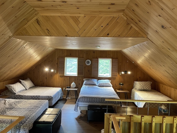Un dormitorio cálido en el ático con paredes de madera y techos inclinados, con dos camas, una mesita y un banco.
