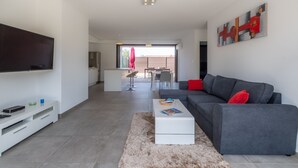 Una sala de estar moderna con un sofá gris, una mesa de centro blanca y un televisor de pantalla plana montado en la pared.