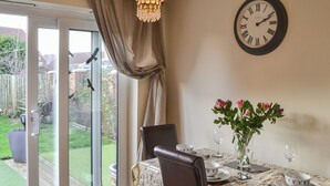 A dining area with a table set for two, a clock on the wall, and a view through a glass door. - 2 bedroom accommodation in Hadston, near Amble (Hadston, near Amble)