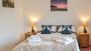 A neatly made bed with towels, two bedside lamps, and wall art depicting a beach scene and a sunset. - 2 bedroom accommodation in Hadston, near Amble (Hadston, near Amble)