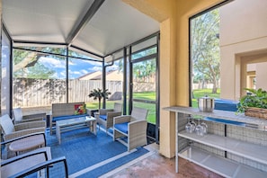 Ein überdachter Patio-Bereich mit Korbmöbeln, einem Tisch und einer Grillstation.
