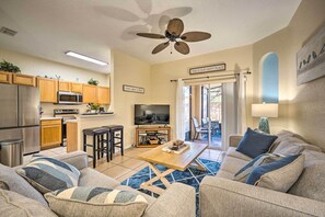 Ein modernes Wohnzimmer mit Sofa, Couchtisch und Fernseher. Es gibt einen Küchenbereich mit Geräten und einen Essbereich mit Tisch und Stühlen.