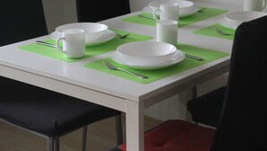 A dining table set with white plates, bowls, and cups on green placemats, with black and red chairs around it. - 1 Studio Flat walking distance to ski lifts (we have 2 in the same building) (Kaprun)