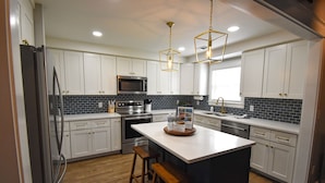 Una cocina moderna con armarios blancos, una isla central, electrodomésticos de acero inoxidable y un salpicadero de azulejos negros.