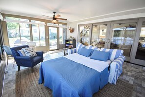 Un dormitorio con una cama grande, una silla, un ventilador de techo y vistas a través de puertas de cristal.
