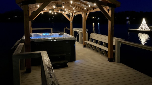 Una terraza de madera con un jacuzzi y un pabellón decorado con luces colgantes.