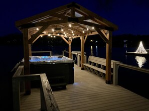 Una terraza de madera con un jacuzzi y un pabellón decorado con luces colgantes.