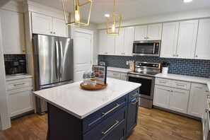 A modern kitchen with white cabinets, stainless steel appliances, and a marble countertop. - Blue Heron Haven - Ultimate Lake Escape: Lake bouncer, Arcade, Kayaks, Hot Tub (Lexington)