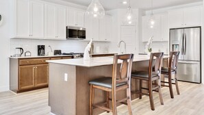 Una cocina moderna con armarios blancos, electrodomésticos de acero inoxidable y una isla central con taburetes de bar.