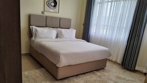Una camera da letto con un letto, una testiera, un quadro appeso al muro e una finestra con tende.