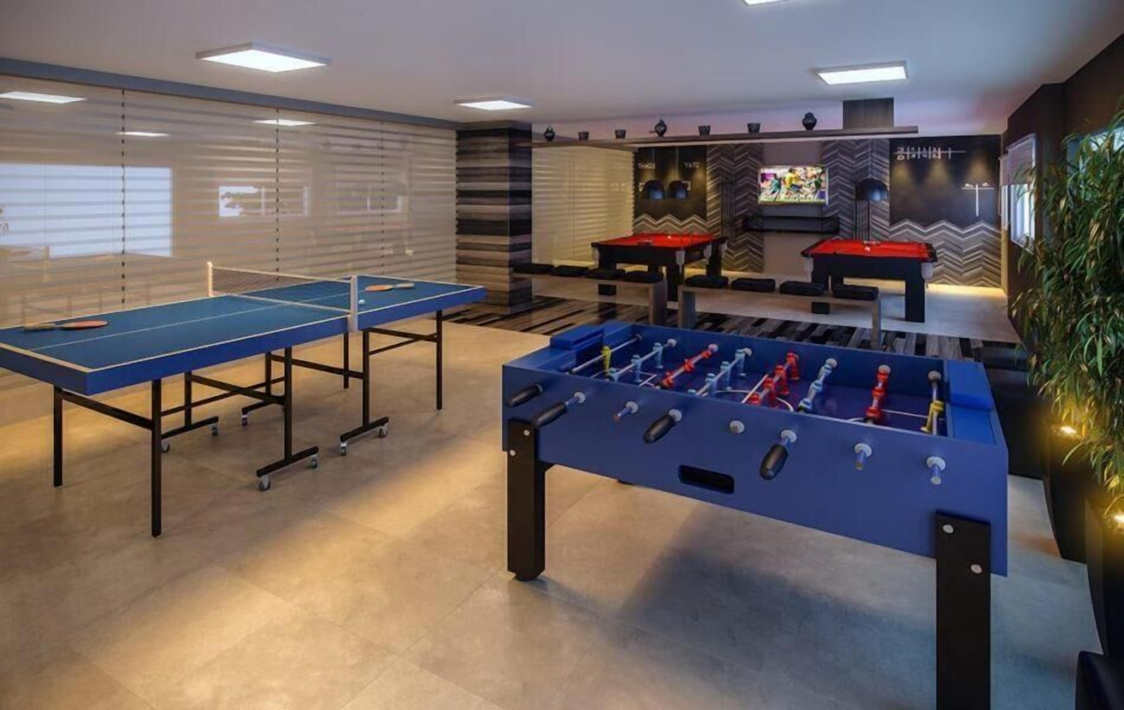 A room with a ping pong table, a foosball table, and two pool tables.