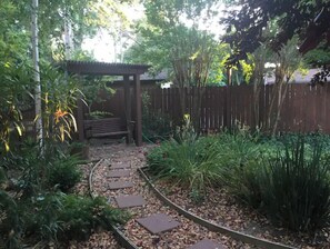 Stroll through the serene garden, surrounded by lush plants and a tranquil pathway leading to a shaded pergola.
