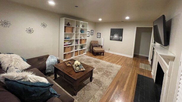 Una sala de estar con un sofá marrón, una mesa de centro de madera, una estantería, una chimenea y un televisor montado en la pared.