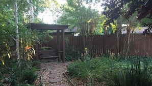 Un sendero en un jardín con piedras para pisar, rodeado de plantas diversas y una pérgola de madera.
