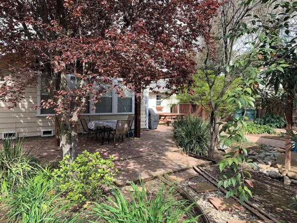 Enjoy al fresco dining under the shade of a tree, surrounded by lush gardens and a patio.