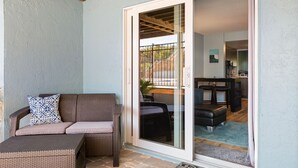 A patio area with a wicker sofa and a sliding glass door leading to an indoor space. - Cozy Beach Escape -saltwater pool - Poolside Suite (Melbourne Beach)