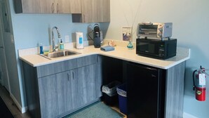 A compact kitchen with a sink, microwave, coffee maker, and a small trash bin. - Cozy Beach Escape -saltwater pool - Poolside Suite (Melbourne Beach)