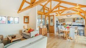 A spacious living area with a high ceiling and exposed wooden beams, a dining area with a round table, and a kitchen in the background. - 2 bedroom accommodation in Horsham (Horsham)