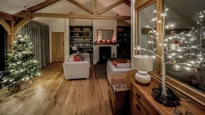 A cozy loft-style room with exposed wooden beams, a white sofa, a small Christmas tree, and a large window with a view of the outside. - 2 bedroom accommodation in Horsham (Horsham)