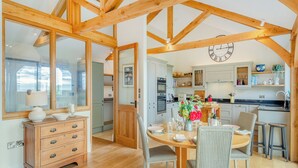 A spacious kitchen with wooden beams, a dining area with a round table, and a view through a glass door. - 2 bedroom accommodation in Horsham (Horsham)