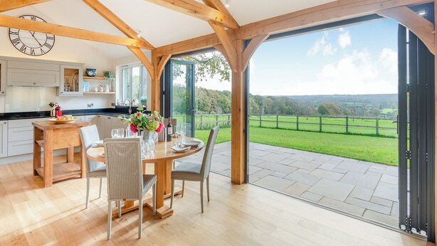 A spacious dining area with a wooden table and chairs, a kitchen with white cabinets, and a large glass door leading to a scenic outdoor view. - 2 bedroom accommodation in Horsham (Horsham)