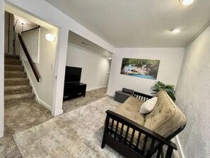 Relax in this stylish living room with a sofa, flat-screen TV, and staircase leading to an upper level.