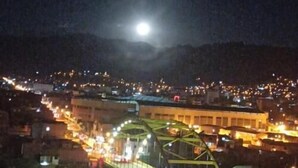 Un paisaje urbano nocturno con un puente y montañas a lo lejos.